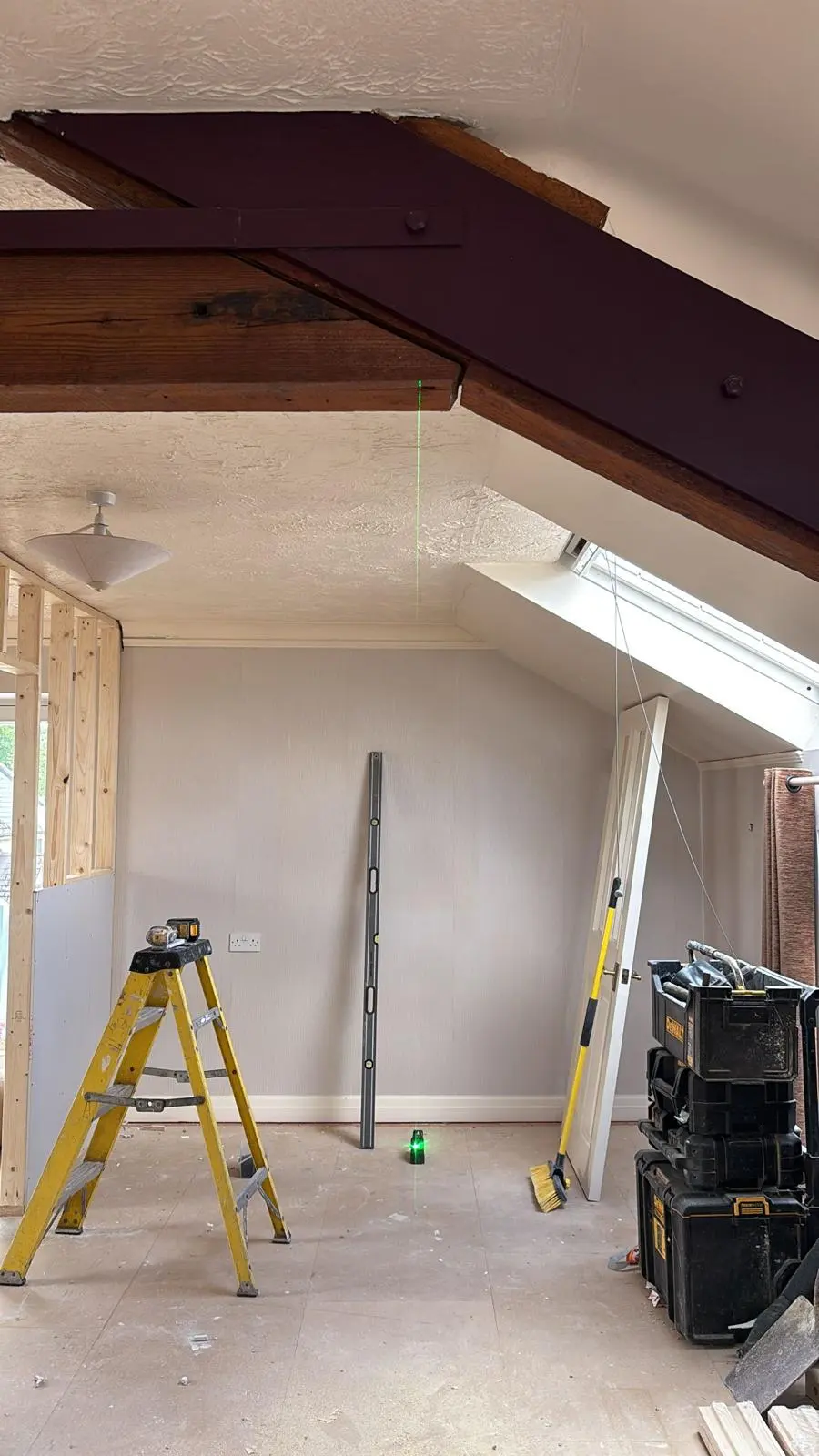Expert structural alterations in progress during a premium Cotswolds property renovation, showing a laser level aligning structural steelwork with exposed heritage timber beams.
