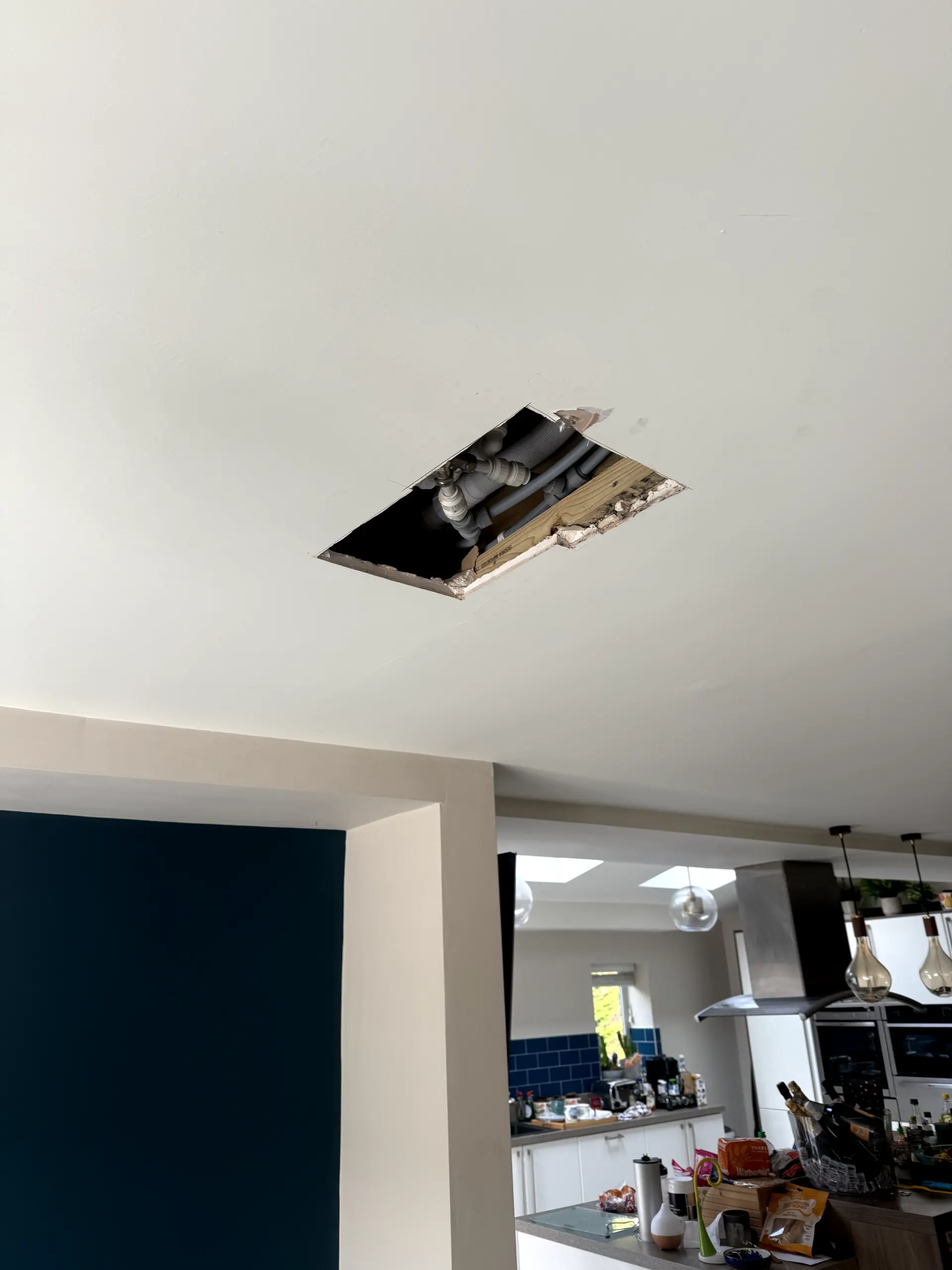 Ceiling access hole revealing plumbing pipes for leak detection and repair services by WGS Services.