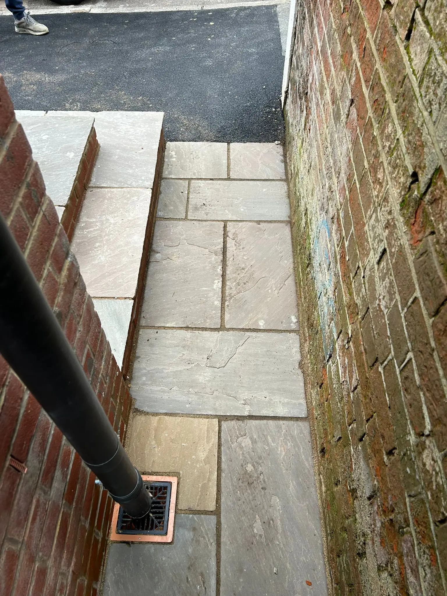 A close-up of a newly laid natural sandstone pathway and step next to a brick wall, showcasing expert paving and hard landscaping.