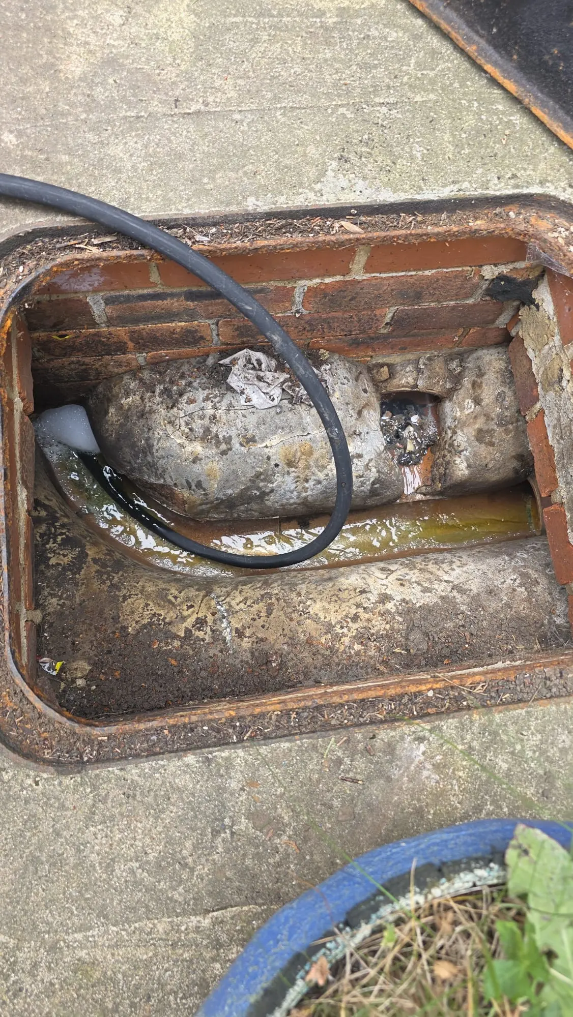 Open brick manhole with a drainage hose inserted, showing flowing water