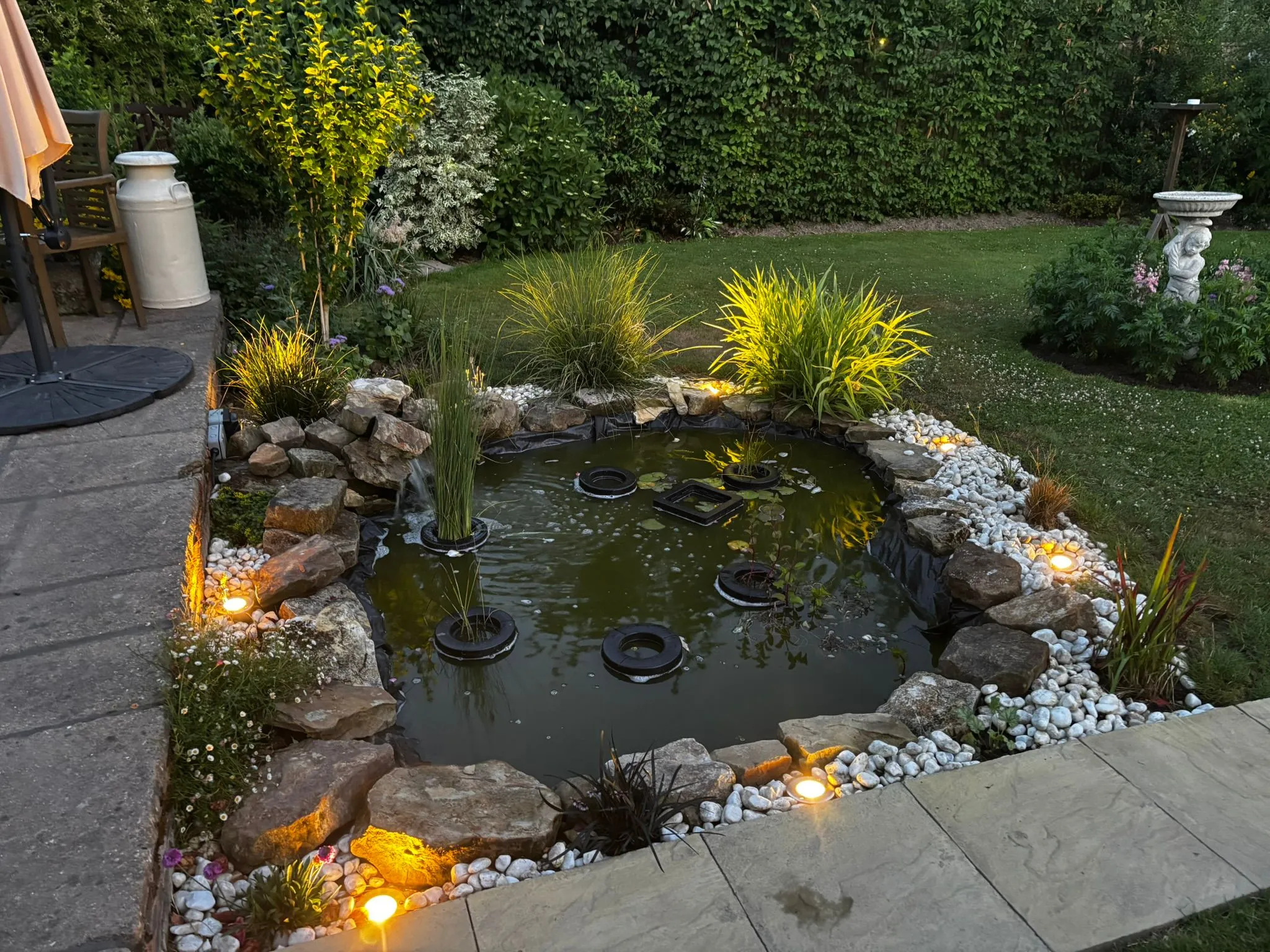 Outdoor garden lighting and pond illumination installed along a stone patio border by Sussex Brown Sparks