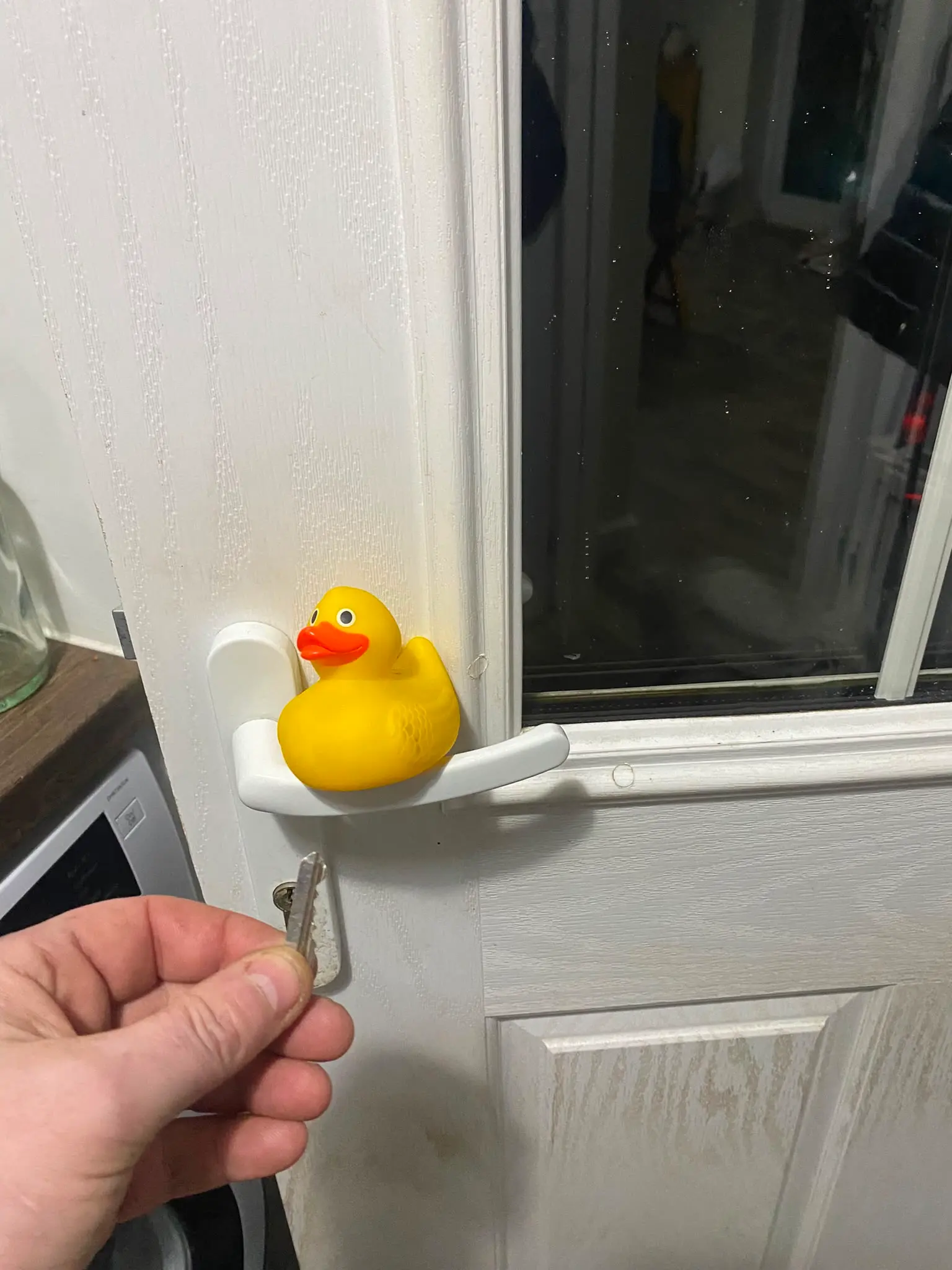 A hand holding a key ready to unlock a white uPVC residential door