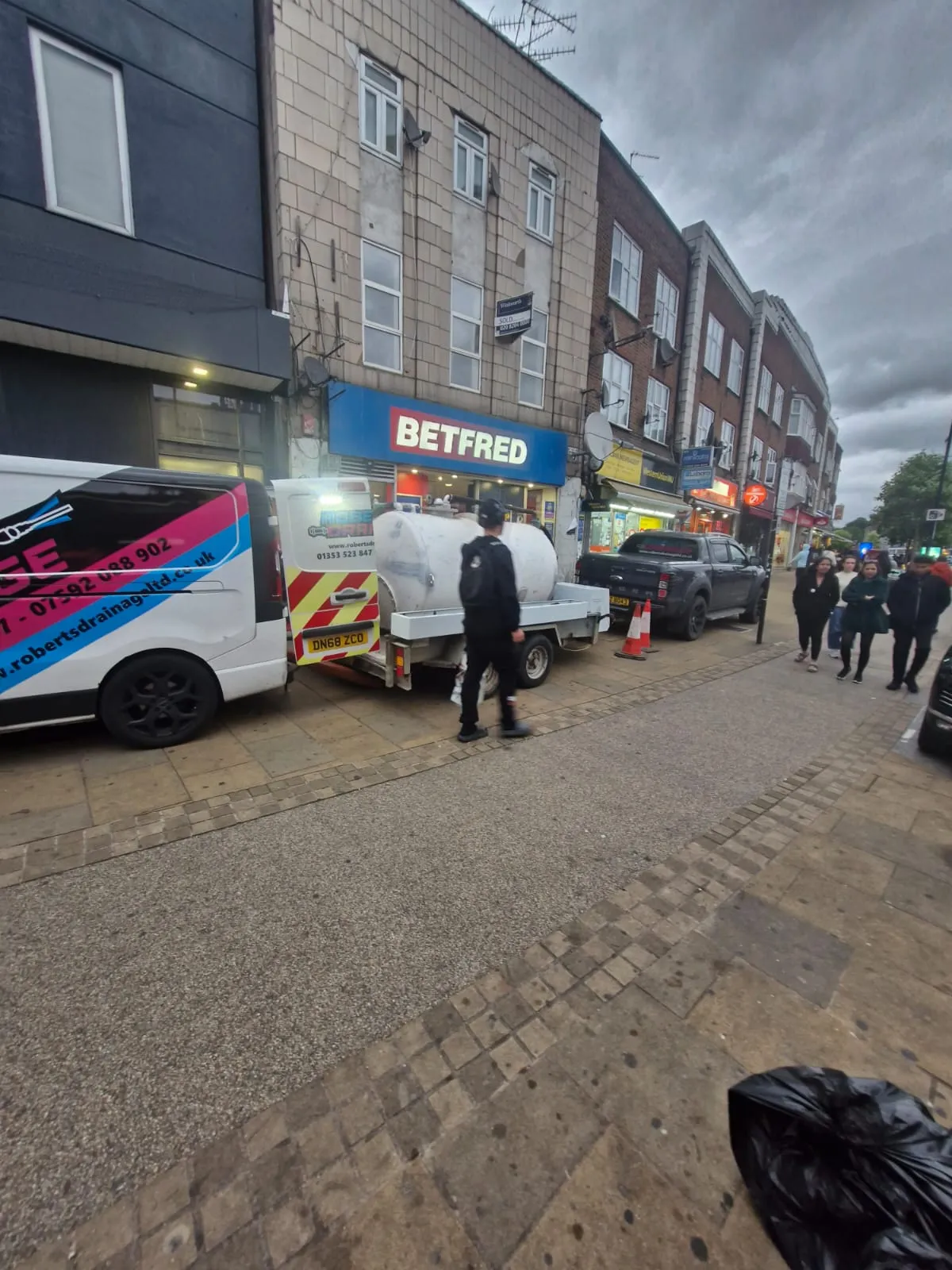 Roberts Drainage Ltd van and liquid waste tanker trailer performing commercial drainage services on a town high street.