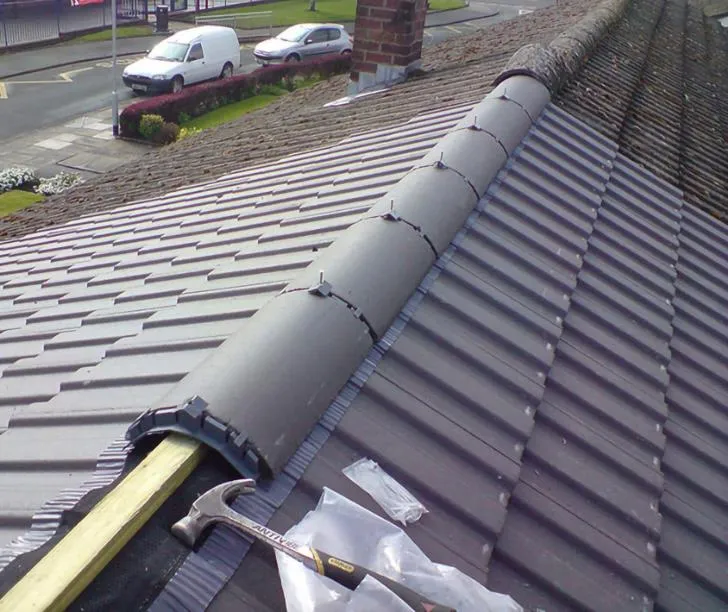 Close-up of a new dry ridge system being installed on a grey tiled roof, with a hammer visible.
