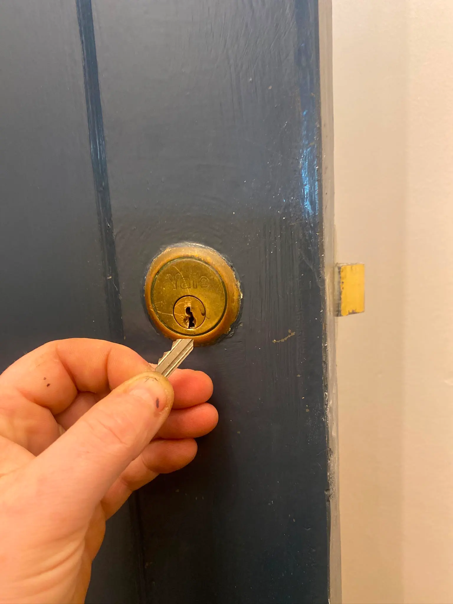 A hand holding a broken key next to a Yale door lock, demonstrating a locksmith emergency requiring snapped key removal.