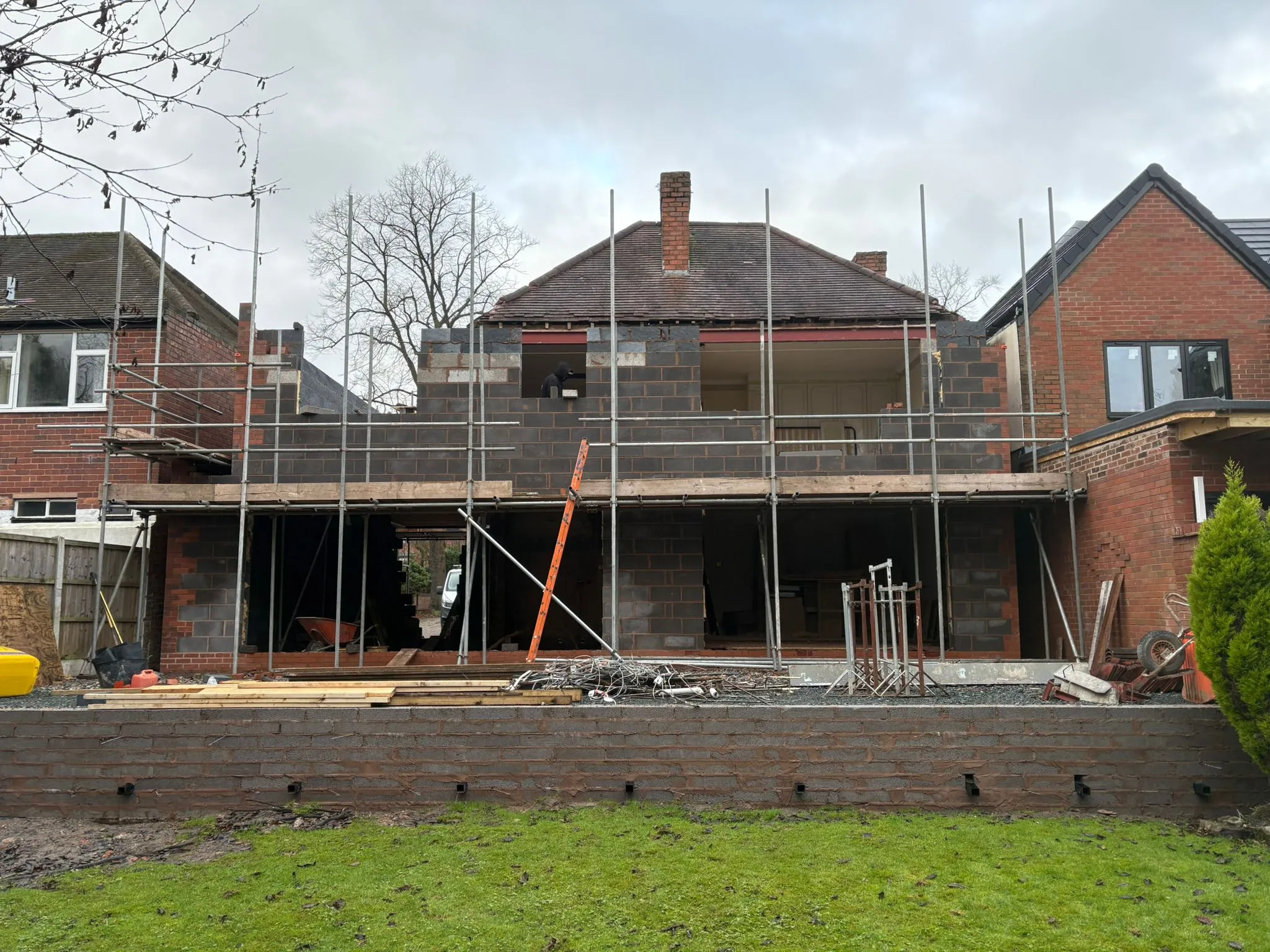 Double-storey home extension under construction with scaffolding around the grey building blocks of the new structure.