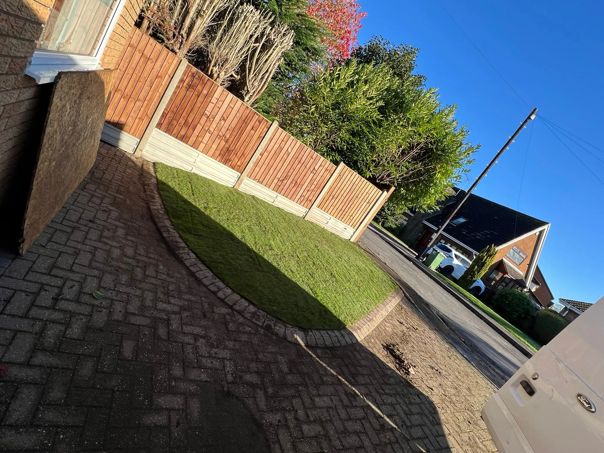 Newly installed wooden fence and green lawn alongside a block paved driveway in a transformed front garden.