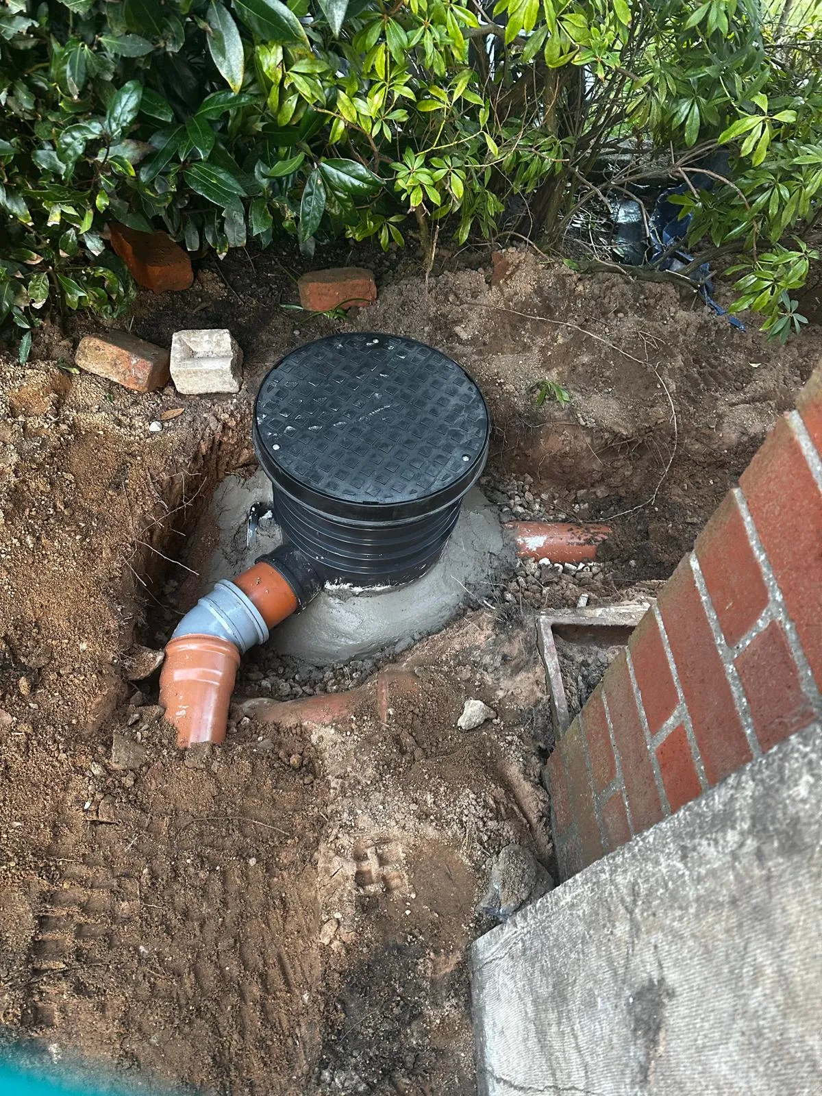 An inspection chamber and orange drainage pipes being installed or repaired in an excavated trench.