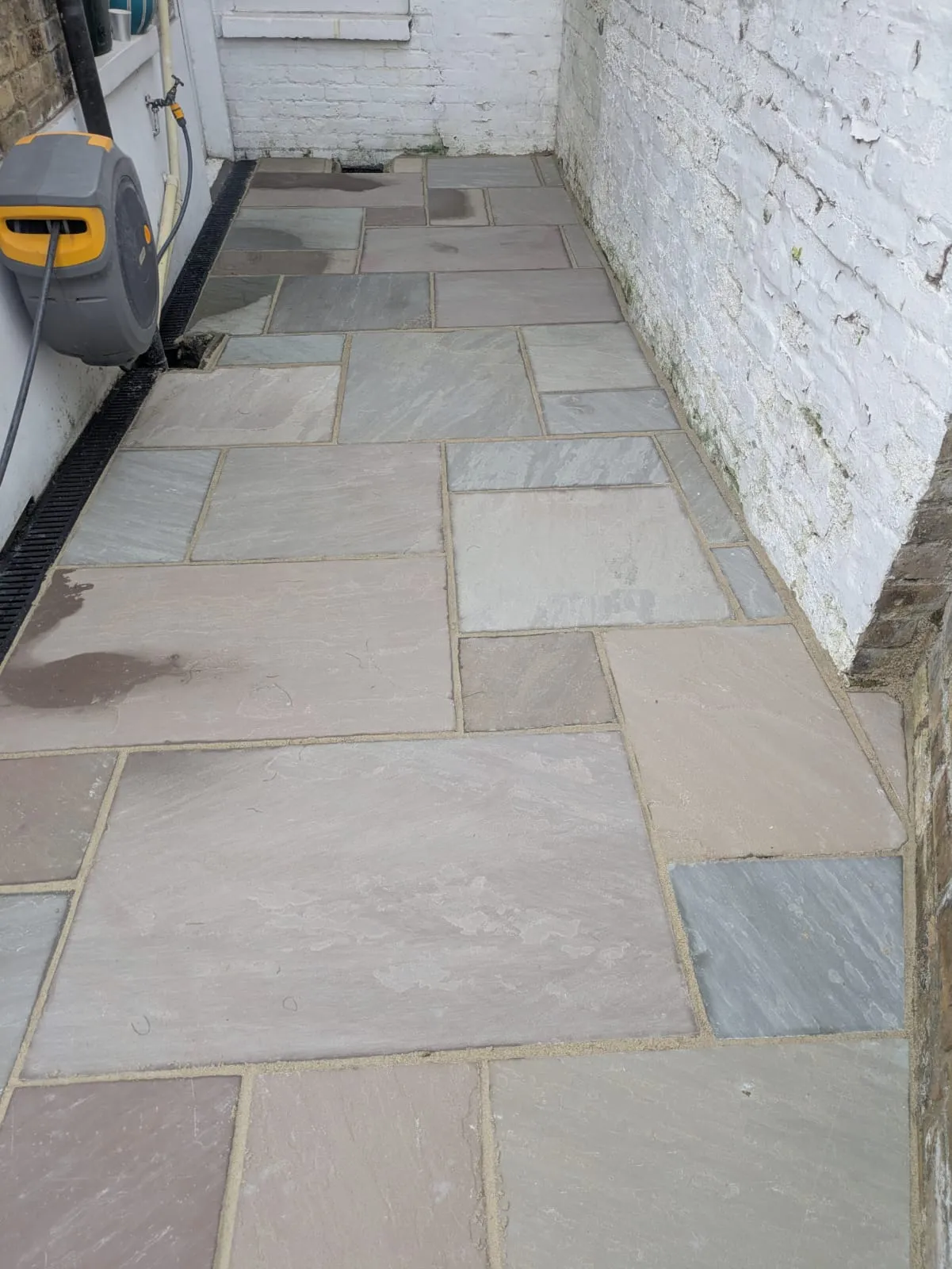 Newly laid Indian sandstone patio or pathway with a drainage channel and white painted brick wall.