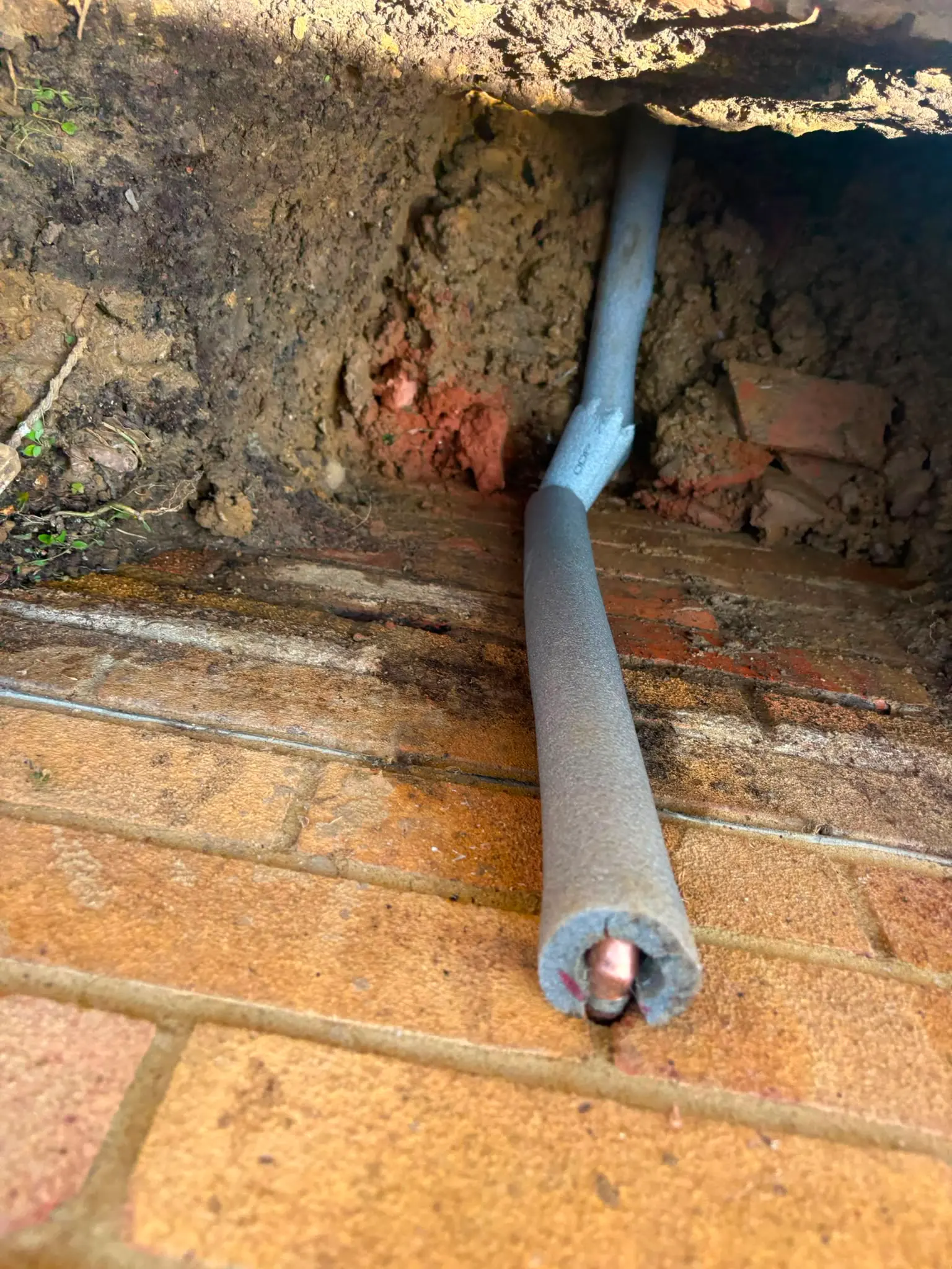 An insulated copper pipe entering a brick wall during pipework excavation and repair
