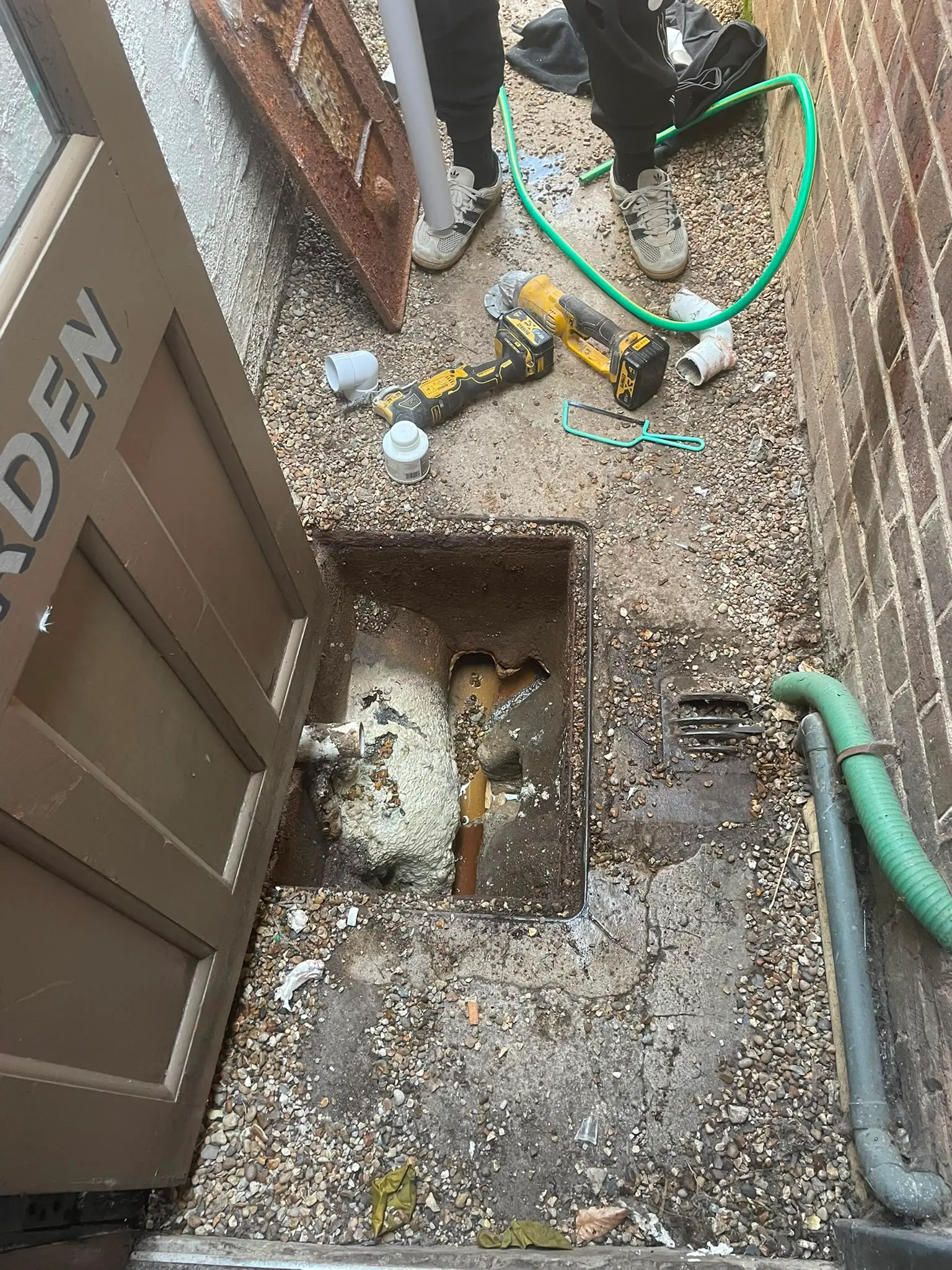 Local Plumbing & Drainage engineer working on an open, damaged outside drain inspection chamber with tools scattered around