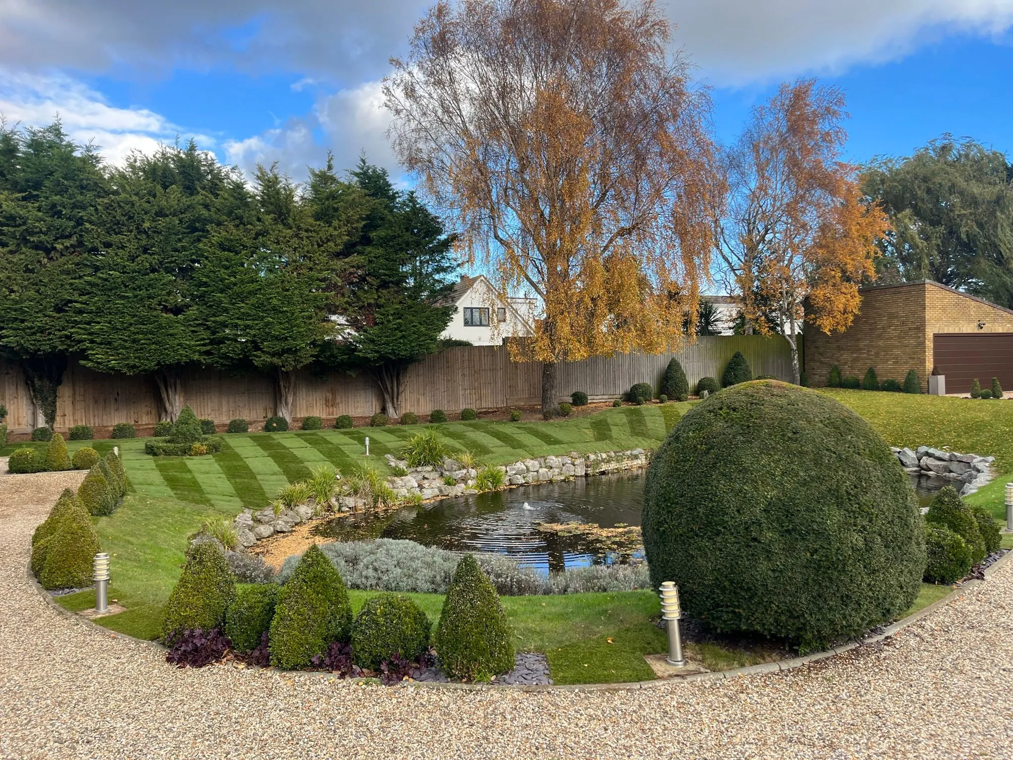 A beautifully landscaped garden with striped turf, a pond, and expert topiary by Foster and Sons Landscaping.