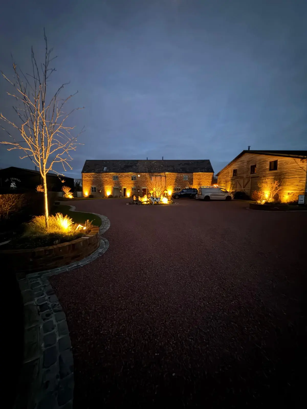 Professional external and driveway lighting installation by JH Electrical Contractors Ltd, showcasing illuminated trees and building facades at night.