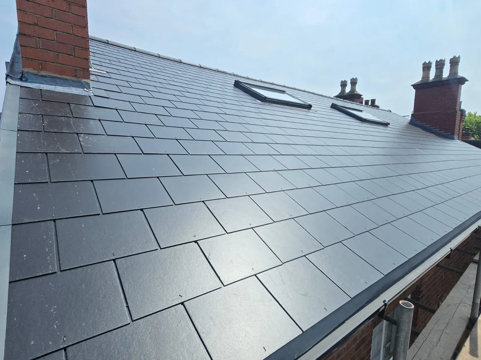 Newly installed dark grey slate tiled roof with two rooflights and a chimney.