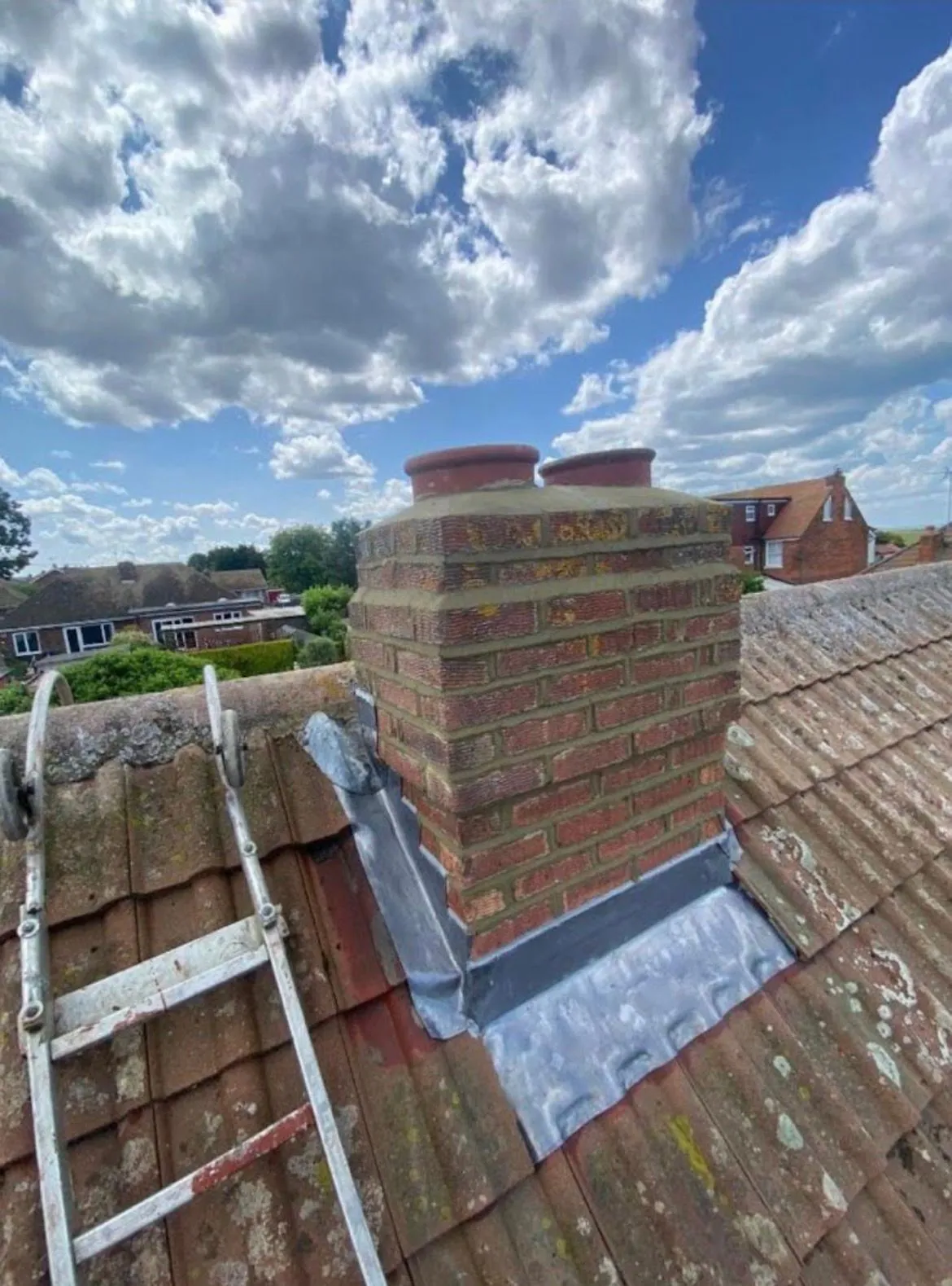 Repointed brick chimney stack with new lead flashing and clay pots on a tiled roof