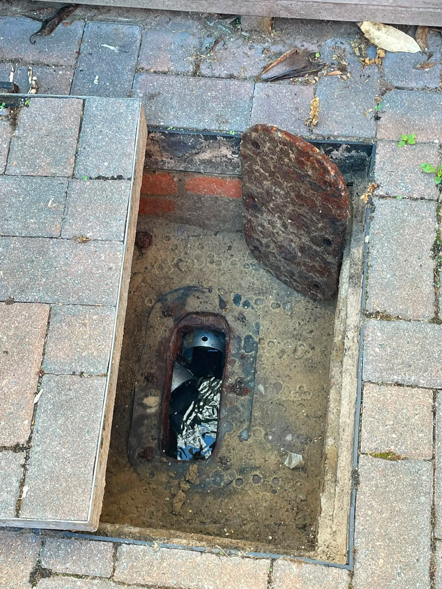 An open block-paved manhole cover revealing an outdoor drainage inspection chamber with standing water inside