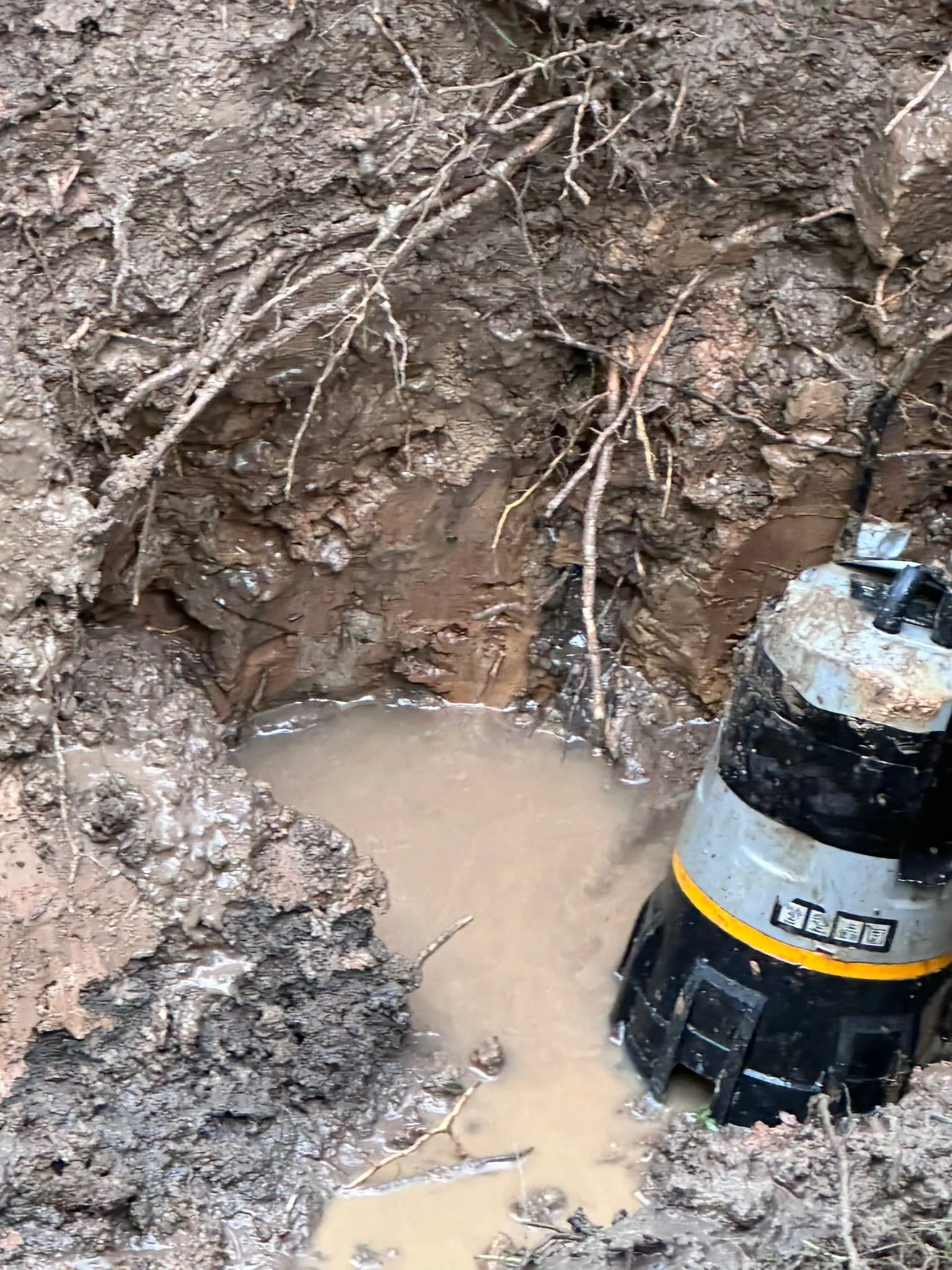 Submersible pump clearing water from a muddy excavation site for professional drainage or water main repairs.