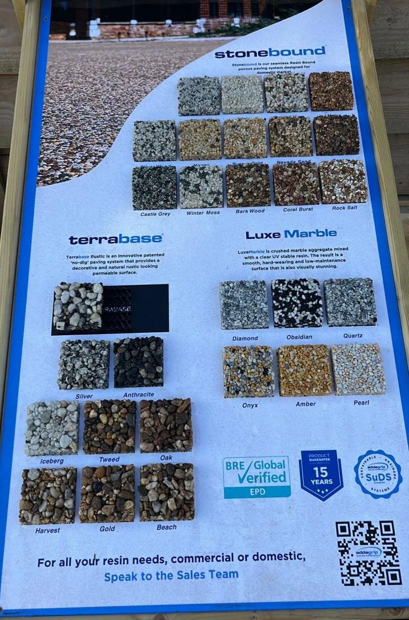 A close-up of a resin driveway sample board, displaying multiple square swatches of different coloured and textured resin-bound aggregates, with product names like 'Castle Grey', 'Diamond', 'Oak', and logos for SUDS compliance and a 15-year guarantee.