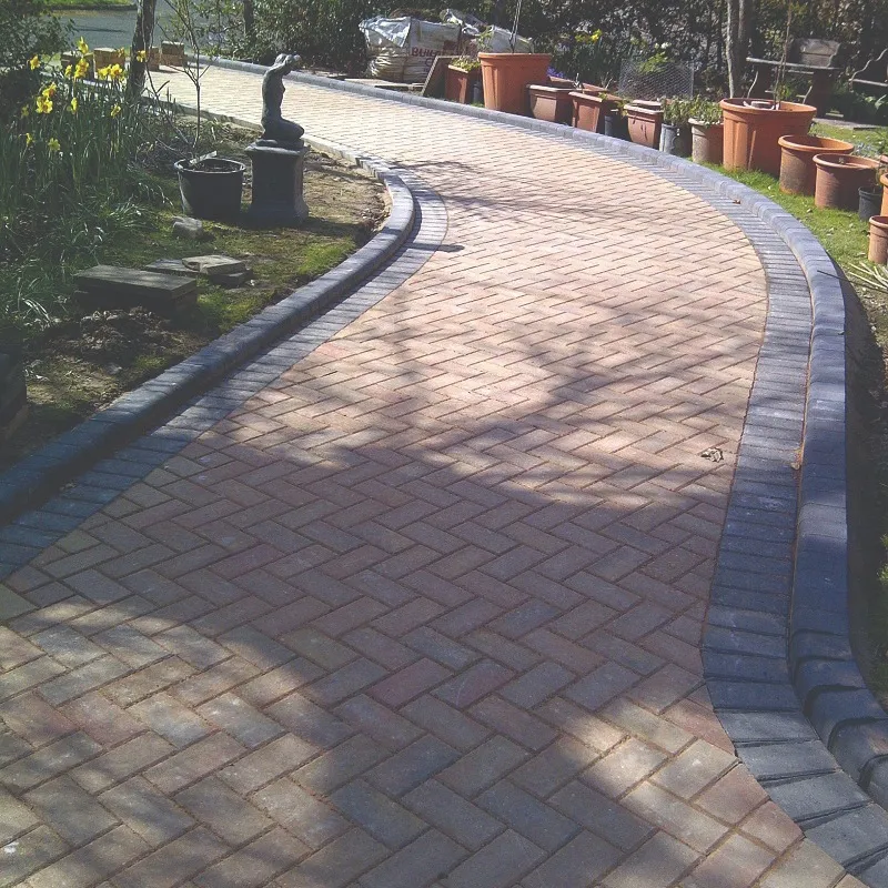 A freshly laid block paving pathway or driveway, curving through a garden with a neatly edged dark border.