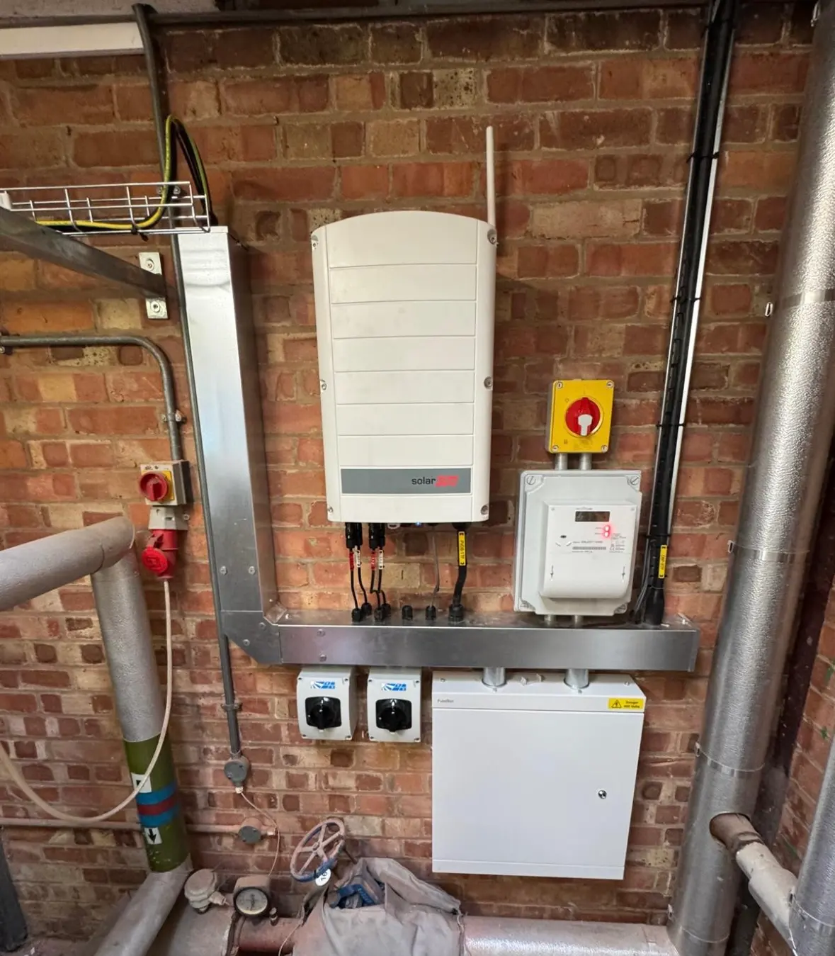 Commercial or industrial electrical installation featuring a solar inverter and metal trunking on a brick wall