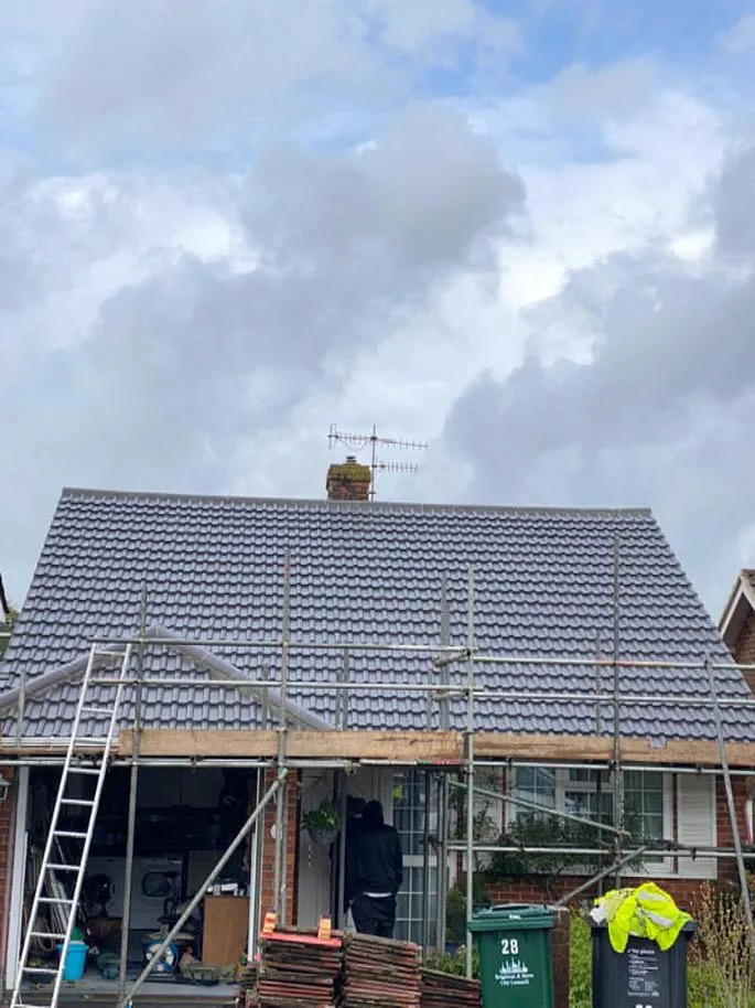 New grey tiled roof installation on a residential property in East Sussex, with scaffolding and a ladder, showcasing re-roofing services.