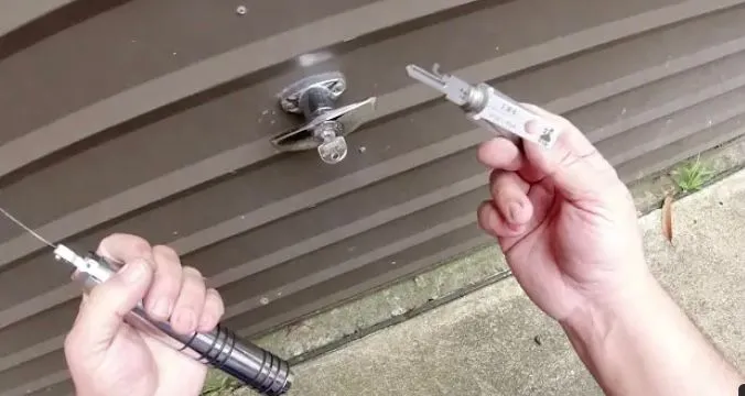 Close-up of a locksmith using professional tools on a T-handle lock, possibly for a garage or shed.