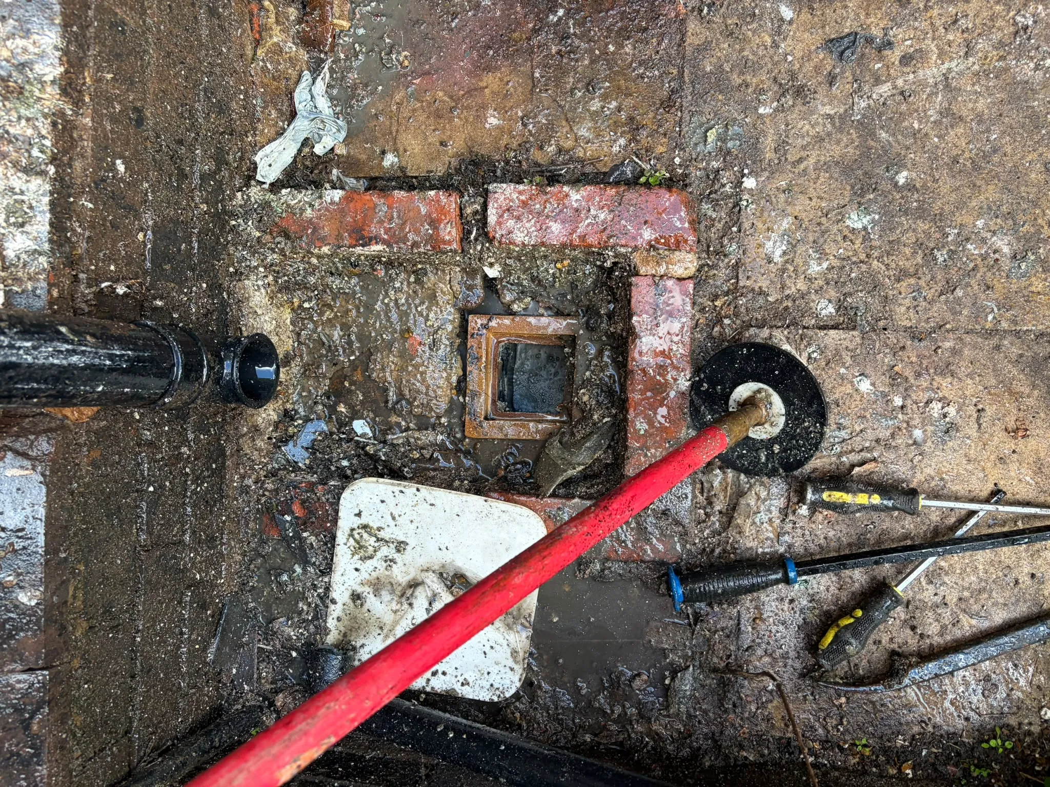 Drain rods and plunger being used to unblock an external drainage gully