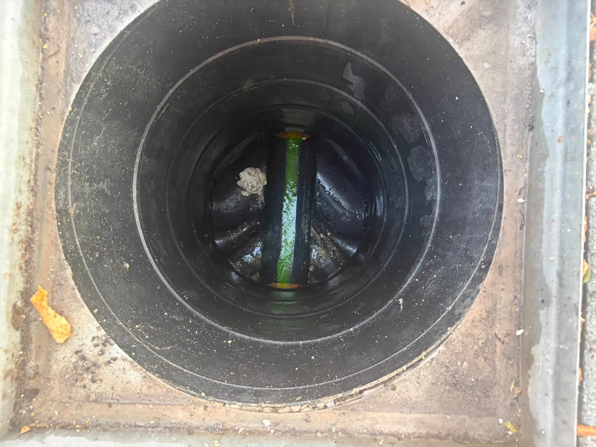 Modern drainage inspection chamber with green tracing dye flowing through the invert channel during an inspection in Slough