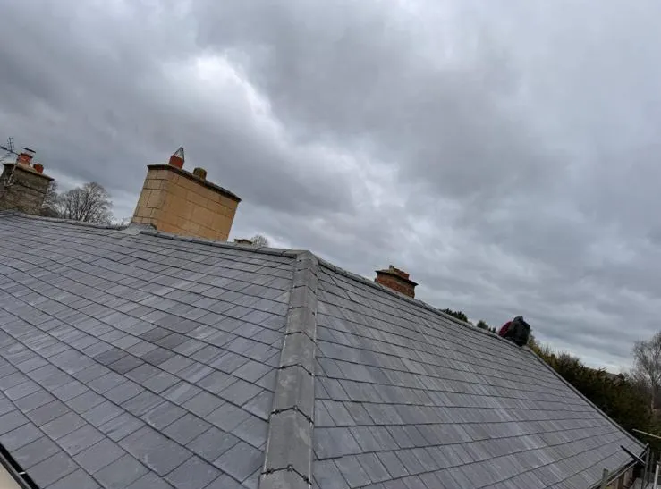 Natural slate hipped roof installation with mortar-free hip ridges and chimney flashing in Plymouth
