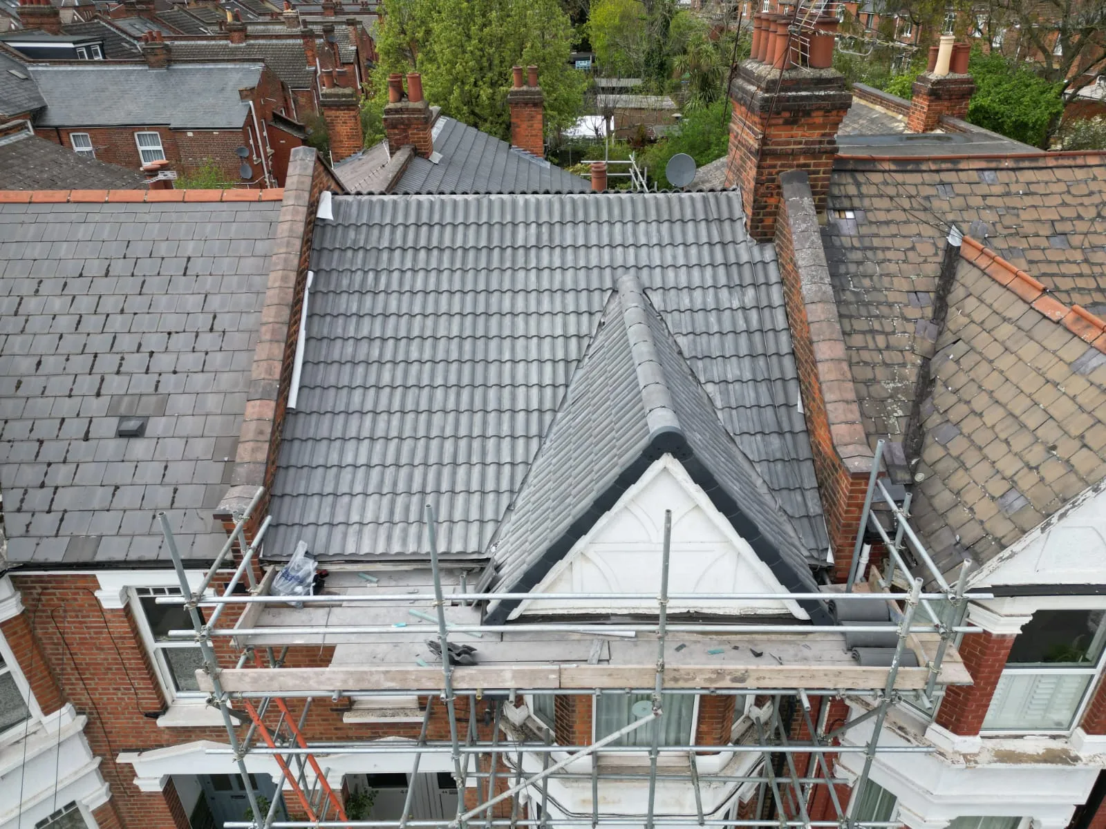 A new grey tiled pitched roof on a residential building, with scaffolding around the dormer window and roofline during re-roofing work.