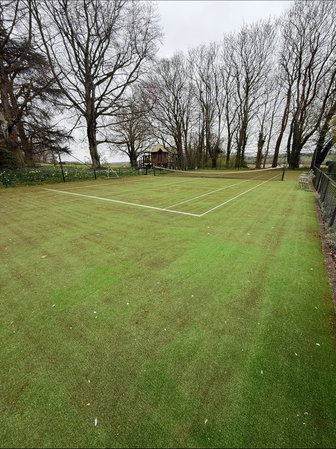 An artificial turf tennis court heavily covered in dirt, moss, and algae before receiving professional sports ground cleaning services.
