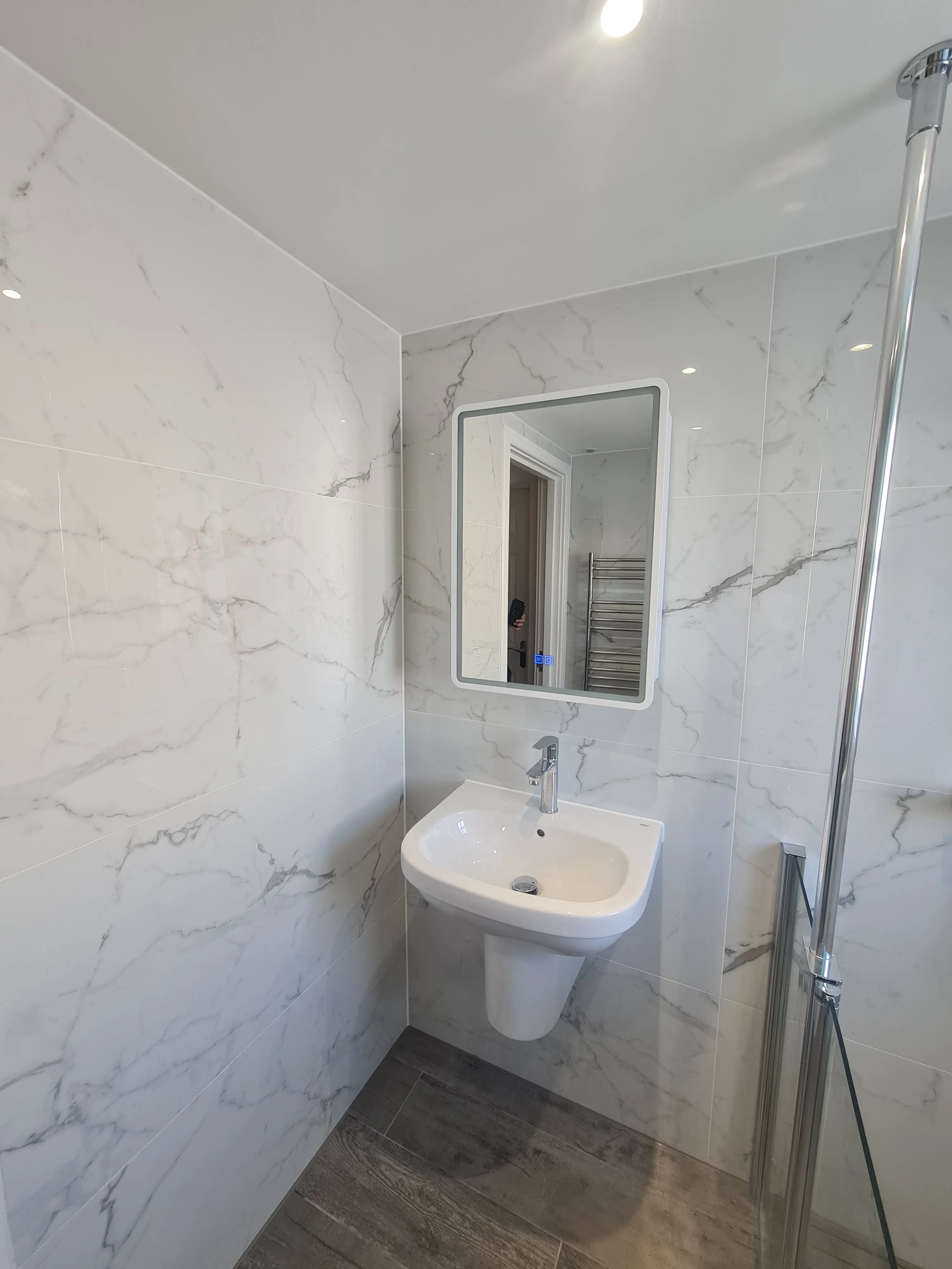 Bespoke luxury bathroom installation in Plymouth featuring marble-effect tiling and an illuminated mirror by Sands & Vossen.