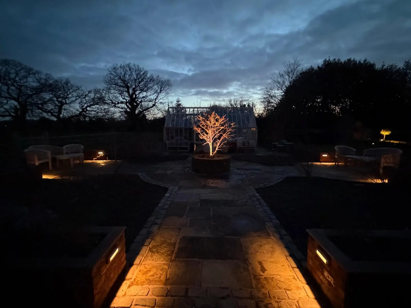 Beautiful external garden lighting illuminating a stone pathway and central tree at dusk in Warrington, showcasing expert outdoor electrical installations by JH Electrical Contractors Ltd.