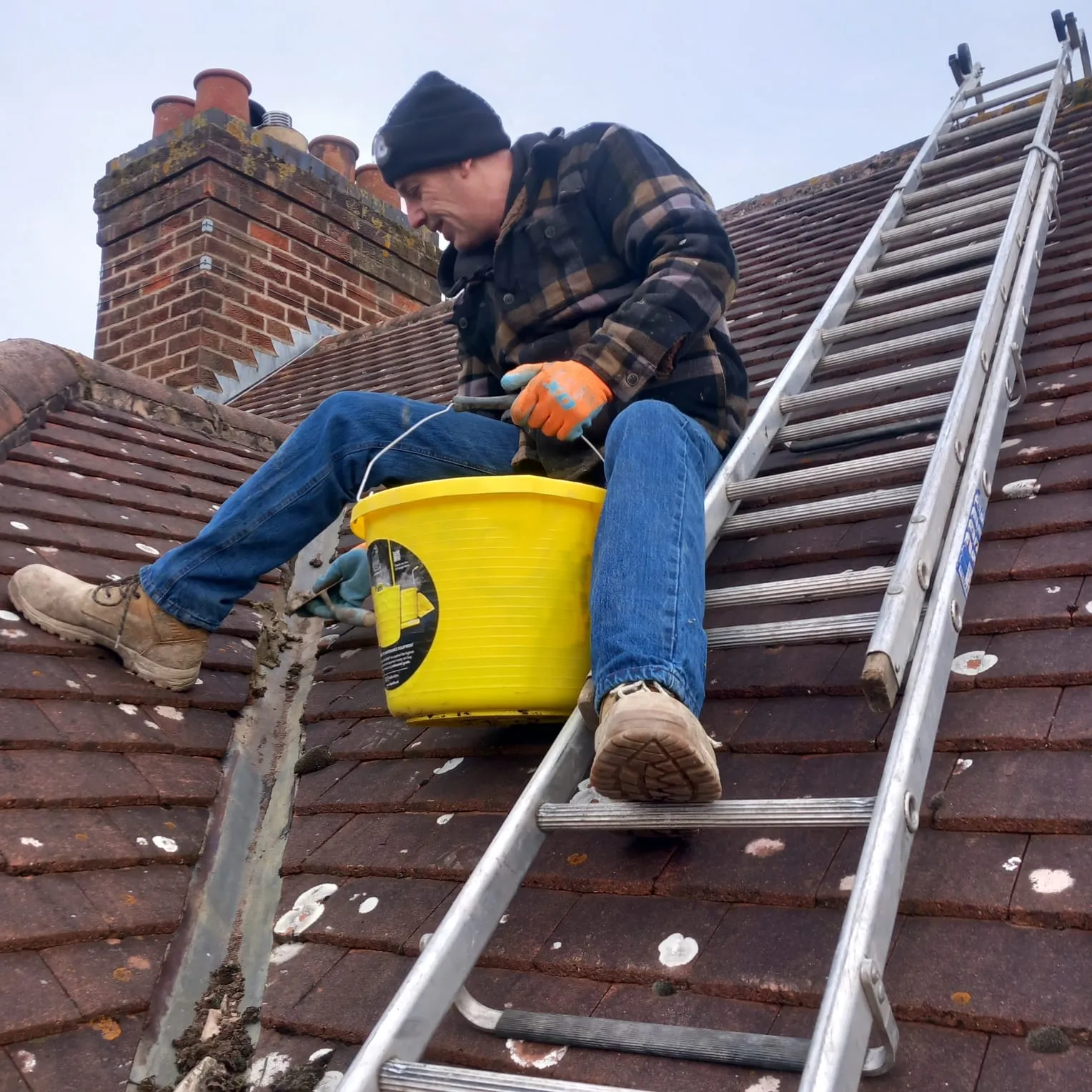 Roofer from 5 Star Roofing Leicester cleaning a roof valley and performing maintenance on a tiled roof near a chimney in Leicester.