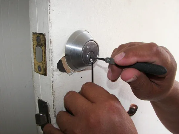 Close-up of a locksmith's hands using tools to pick a deadbolt lock on a white door during a lockout service.