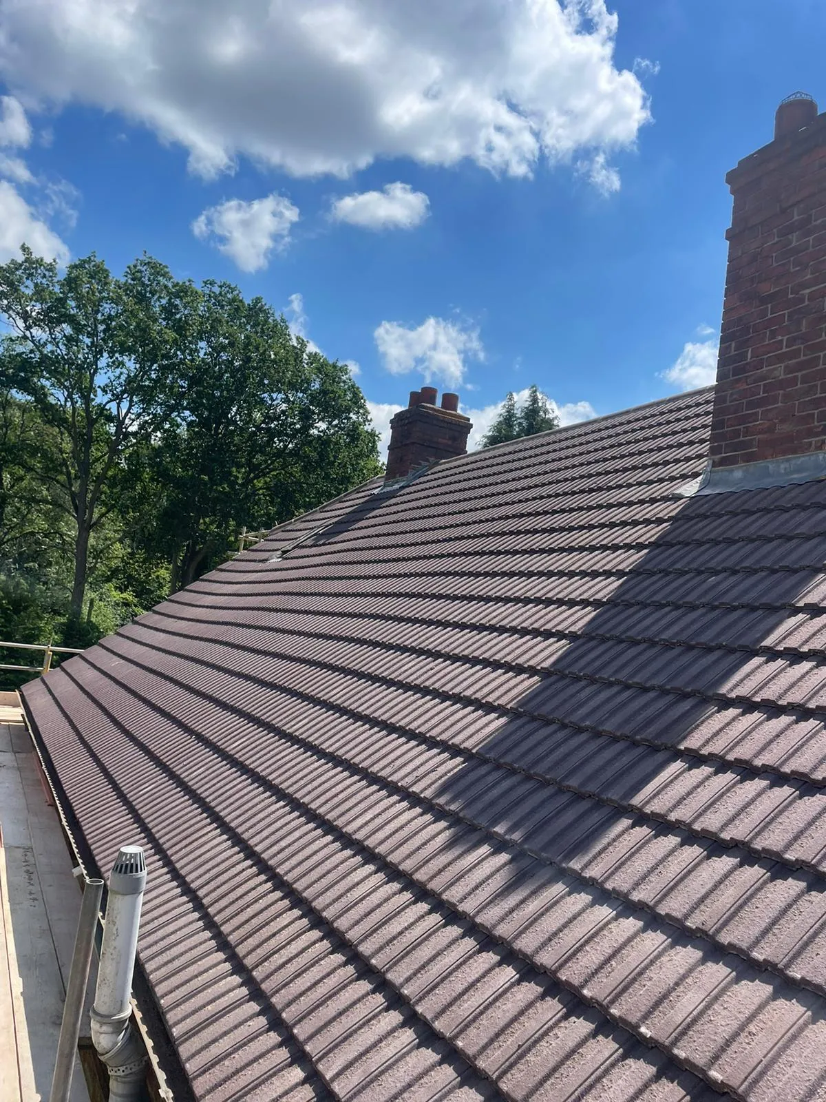 High-quality new brown tiled roof with brick chimneys under a blue sky.