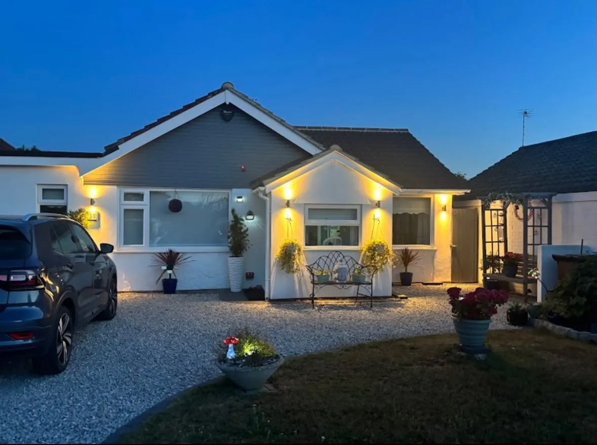 Exterior feature lighting and outdoor wall lights installed on a residential bungalow at dusk