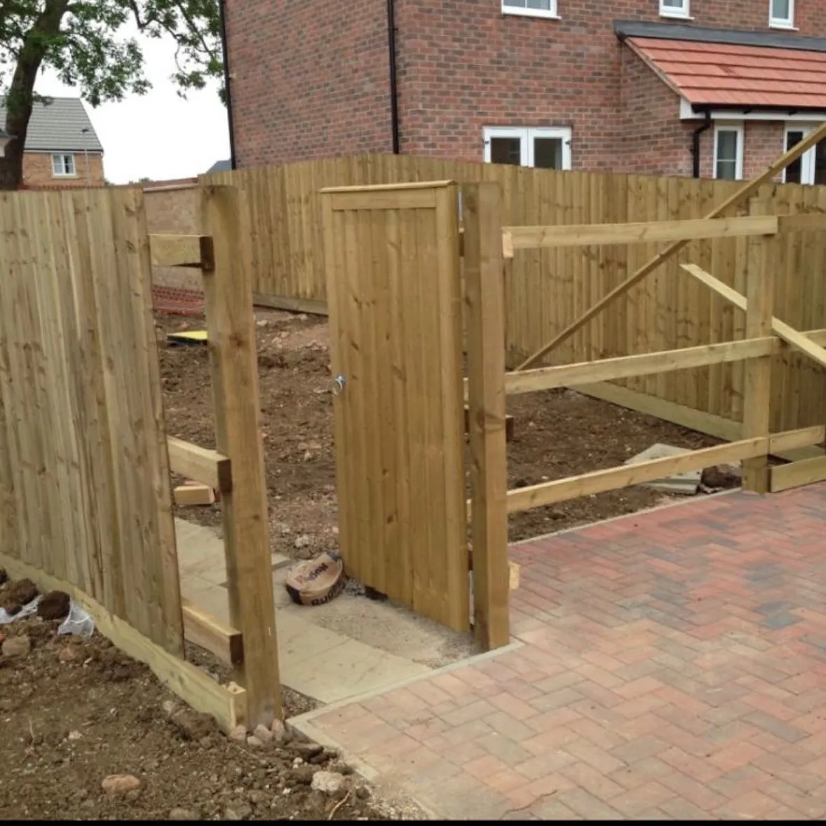 A new wooden garden fence and gate next to a block paved patio, with the garden area beyond still being prepared.