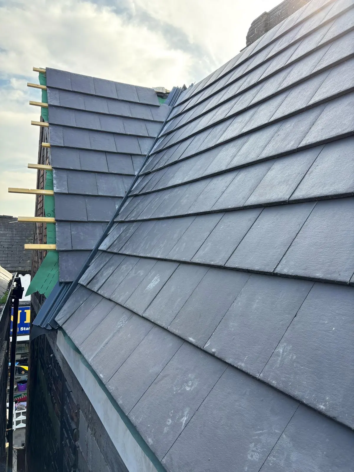 New slate roof installation in progress showing overlapping grey slates, wooden battens, and green roofing felt