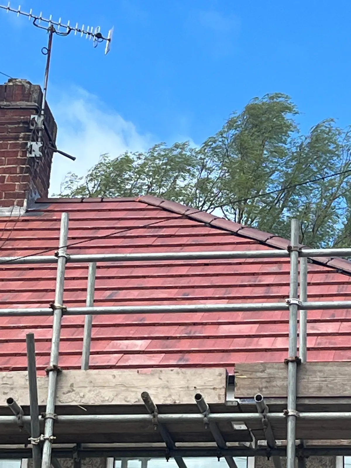 Newly installed red clay tiles on a pitched roof with construction scaffolding in South Yorkshire