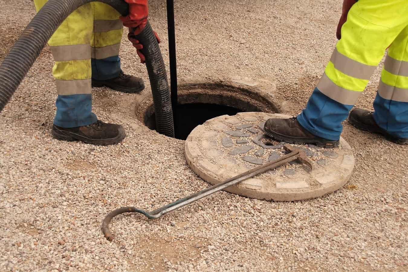 Drain Medics engineers in high-visibility gear using a high-pressure water jetting hose to clear an open manhole drain