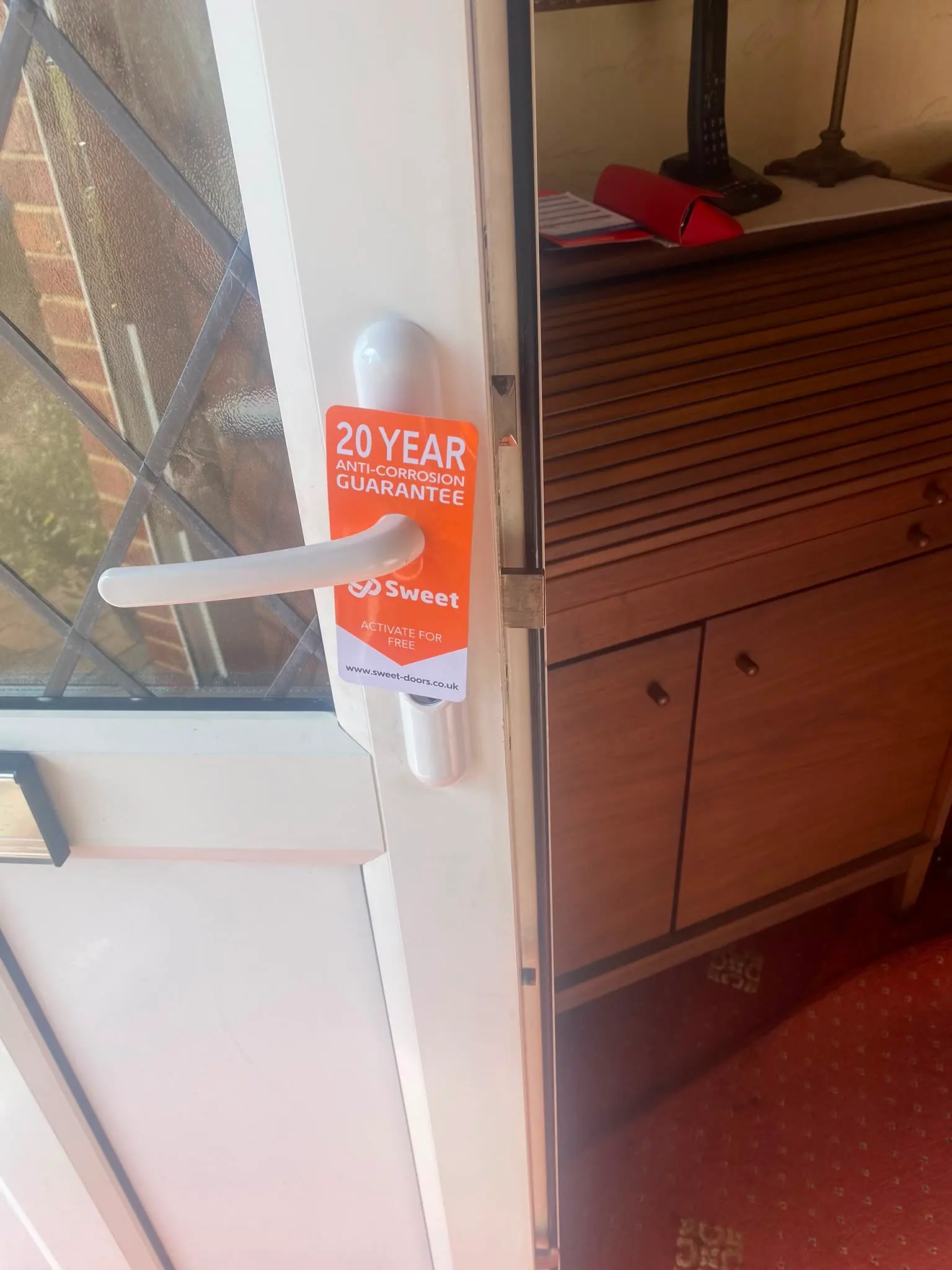 Newly installed white uPVC door handle with a 20-year anti-corrosion guarantee tag fitted to a residential door
