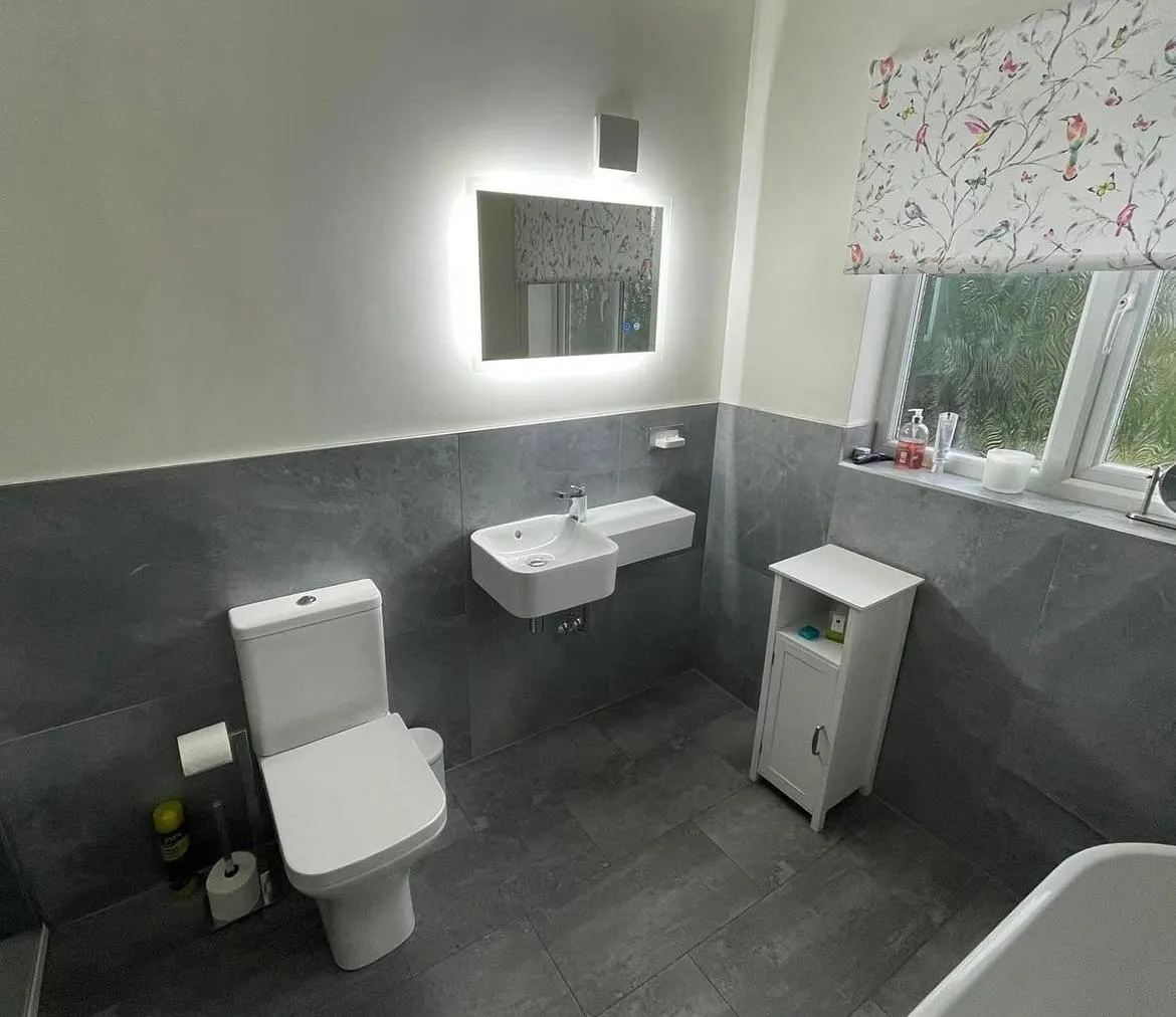 Modern bathroom renovation in York with grey tiling and backlit mirror installed by HM Bathroom and Heating.