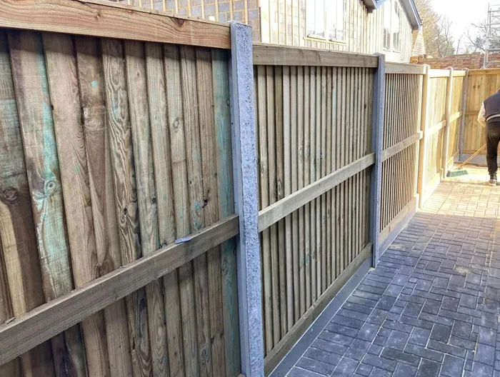 Close-up of new wooden garden fencing with concrete posts next to a clean, block-paved path.