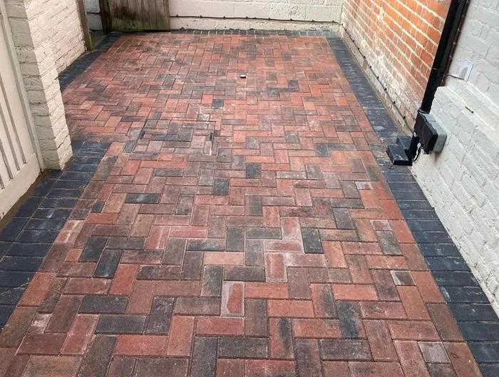 Newly installed block paved driveway in a herringbone pattern with red and grey blocks and a dark border.