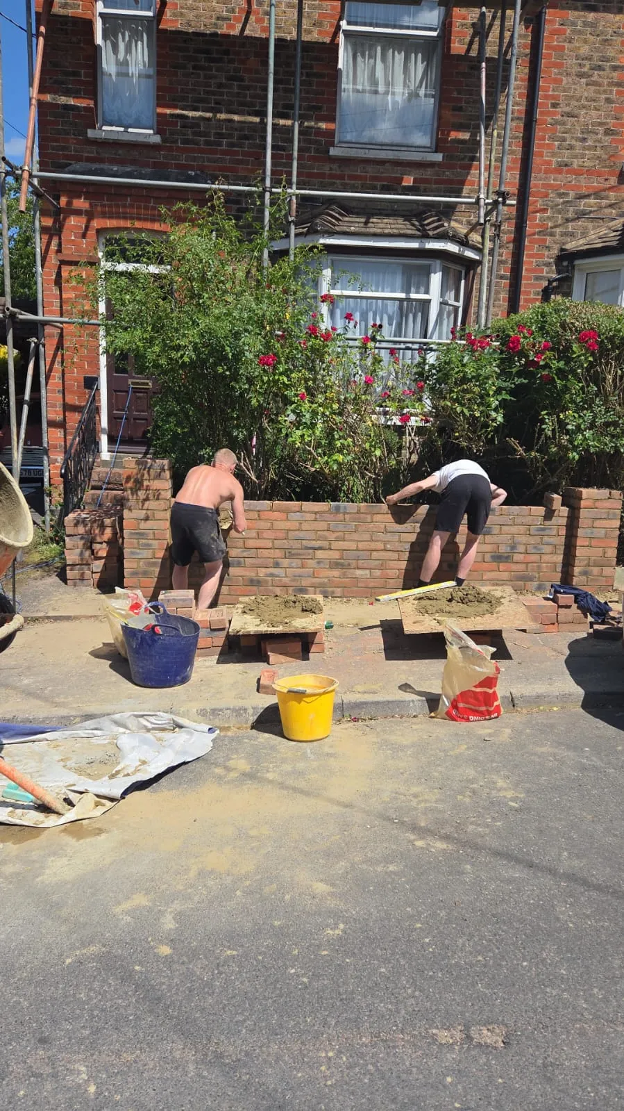Bricklayers building a new garden wall in front of a house