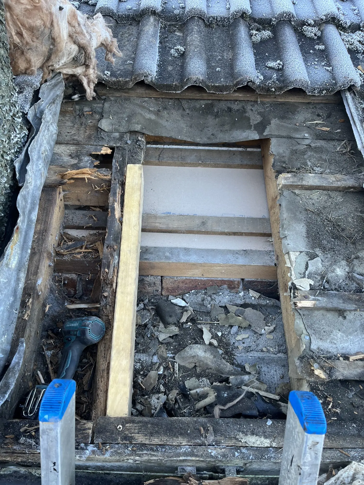 Close-up of an ongoing roof repair showing exposed timber structure, a drill, and a ladder on a tiled roof.