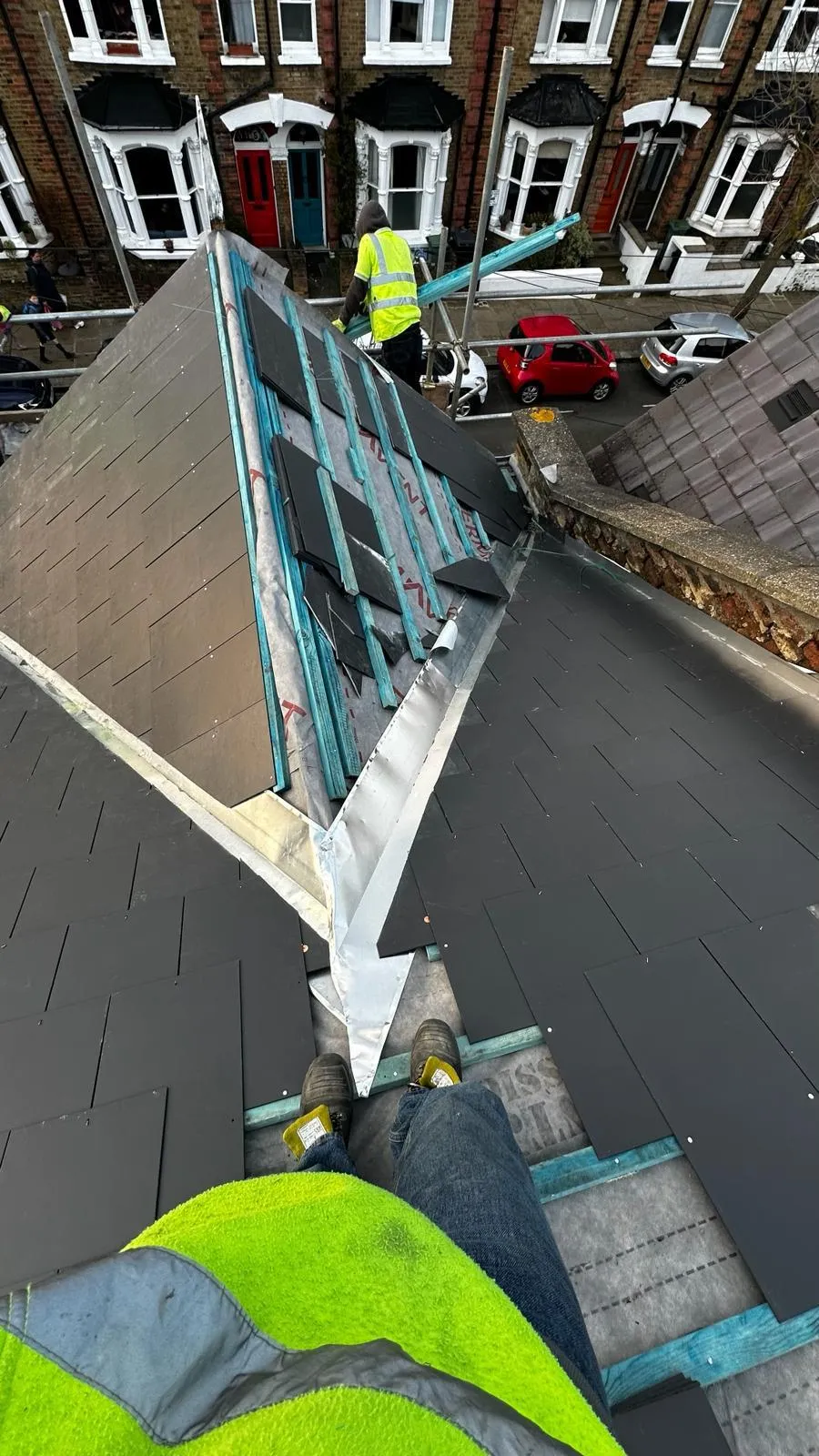 Roofer fitting new slate tiles and valley flashing on a pitched roof of a Victorian terraced property