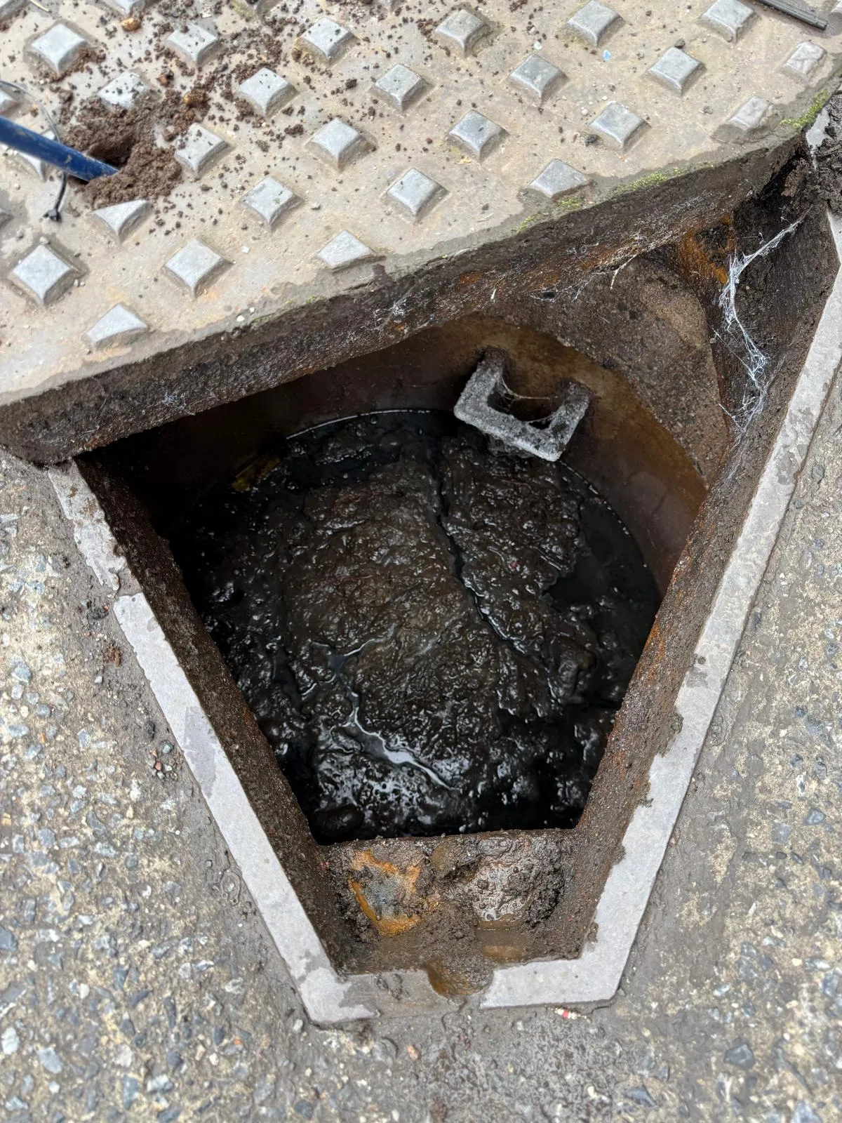 A severely blocked external drain or manhole, overflowing with thick, dark sludge and debris.