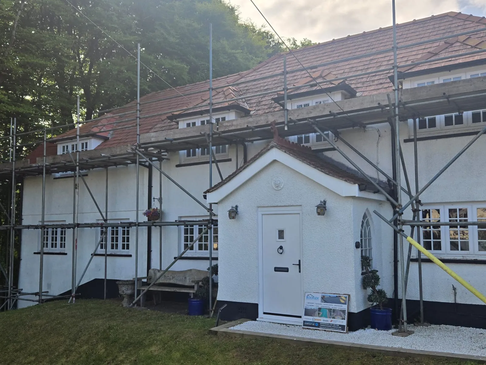 A white residential house with a red tiled roof fully scaffolded for a re-roofing or major exterior renovation project by Rooflex Roofing Solutions.